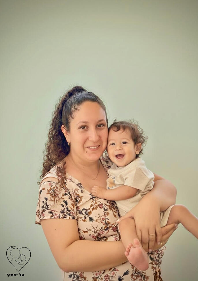 אישה מחייכת מחזיקה תינוק בזרועותיה על רקע בהיר. ליווי התפתחותי והדרכת הורים.